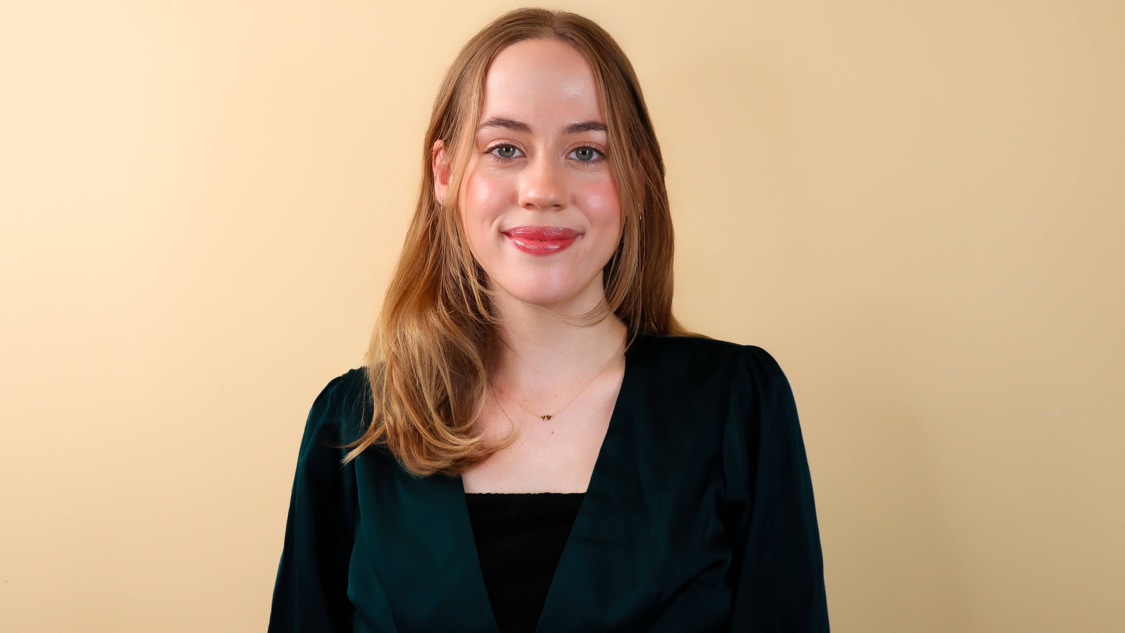Hannah Schmidt wears a black blazer over a black shirt while smiling in front of a beige background. Hannah Schmidt wears a black blazer over a black shirt while smiling in front of a beige background.